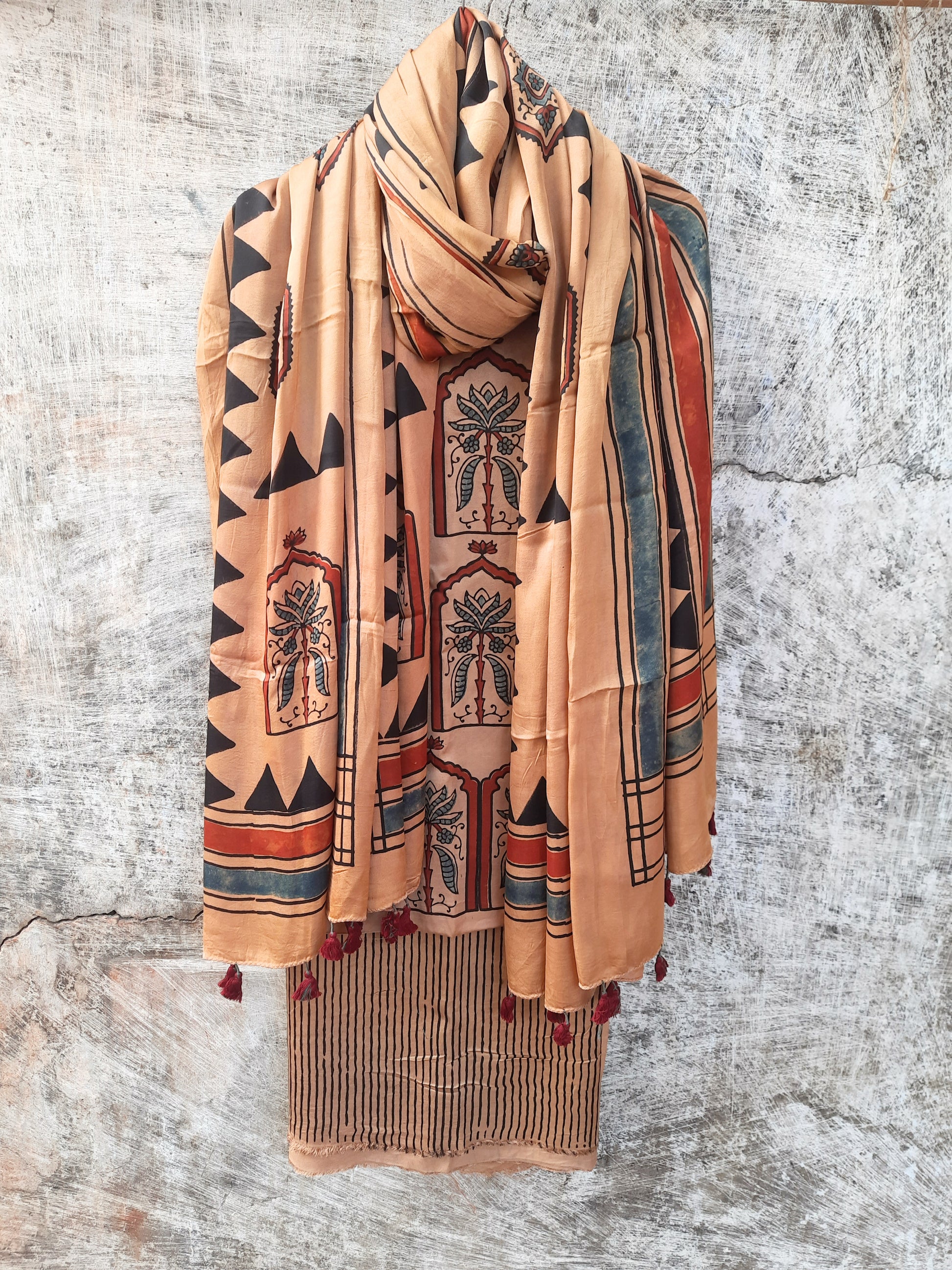 Earthy peach modal silk 3-piece unstitched suit set with Ajrakh hand block prints, natural dye, and tassel-accented stole. Handcrafted and eco-friendly design.