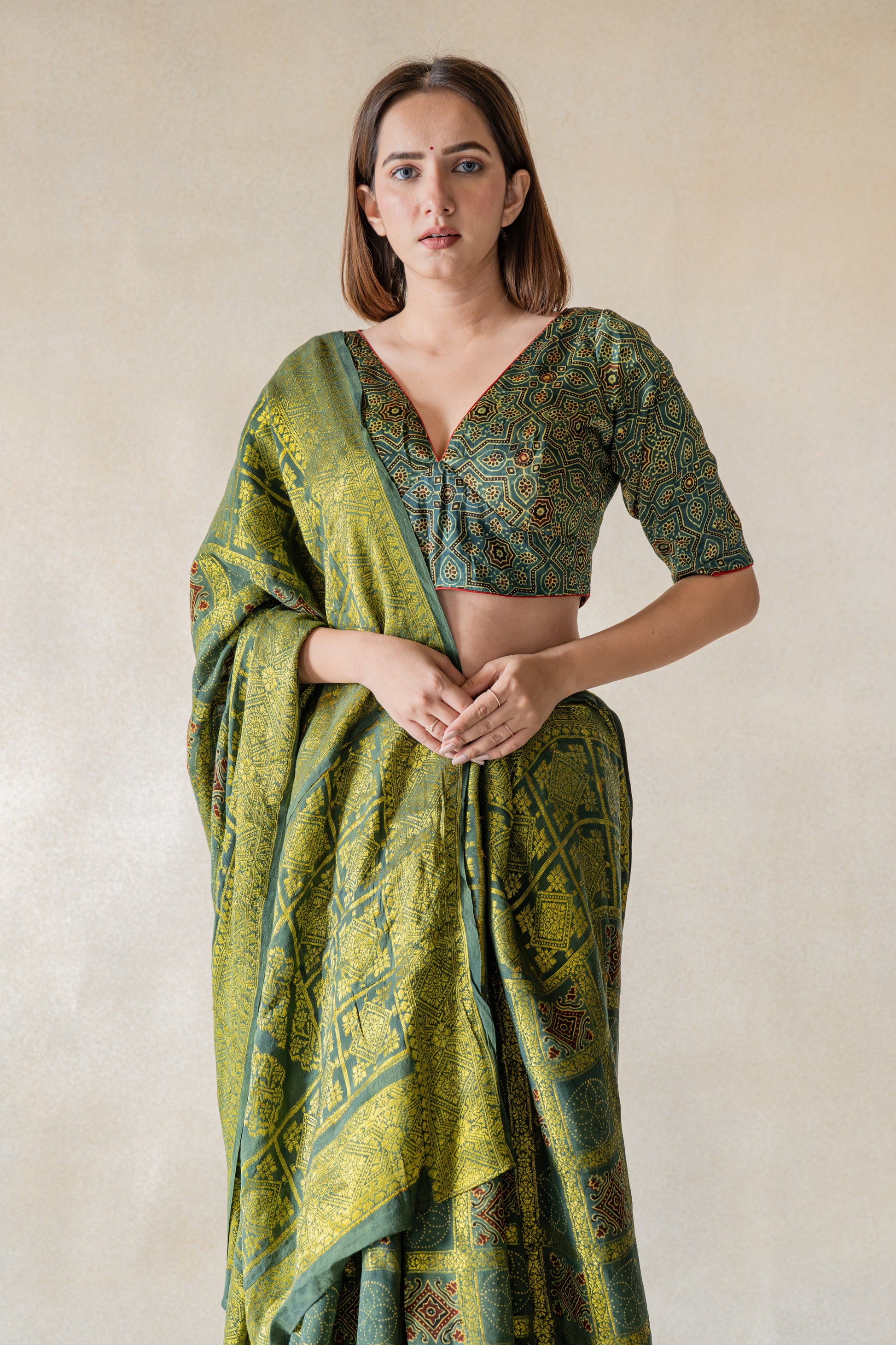 Indulge in luxury with our Green - Ajrakh Modal Silk Blouse. Handcrafted with authentic ajrakh hand block printing and natural green dyes, this blouse exudes elegance. The luxurious and comfort blend of modal silk and pure cotton lining ensure breathability and style. Slow made with intricate details, it features a charming V neck in front and button closure in the back. An exclusive piece for those who appreciate sophistication.
