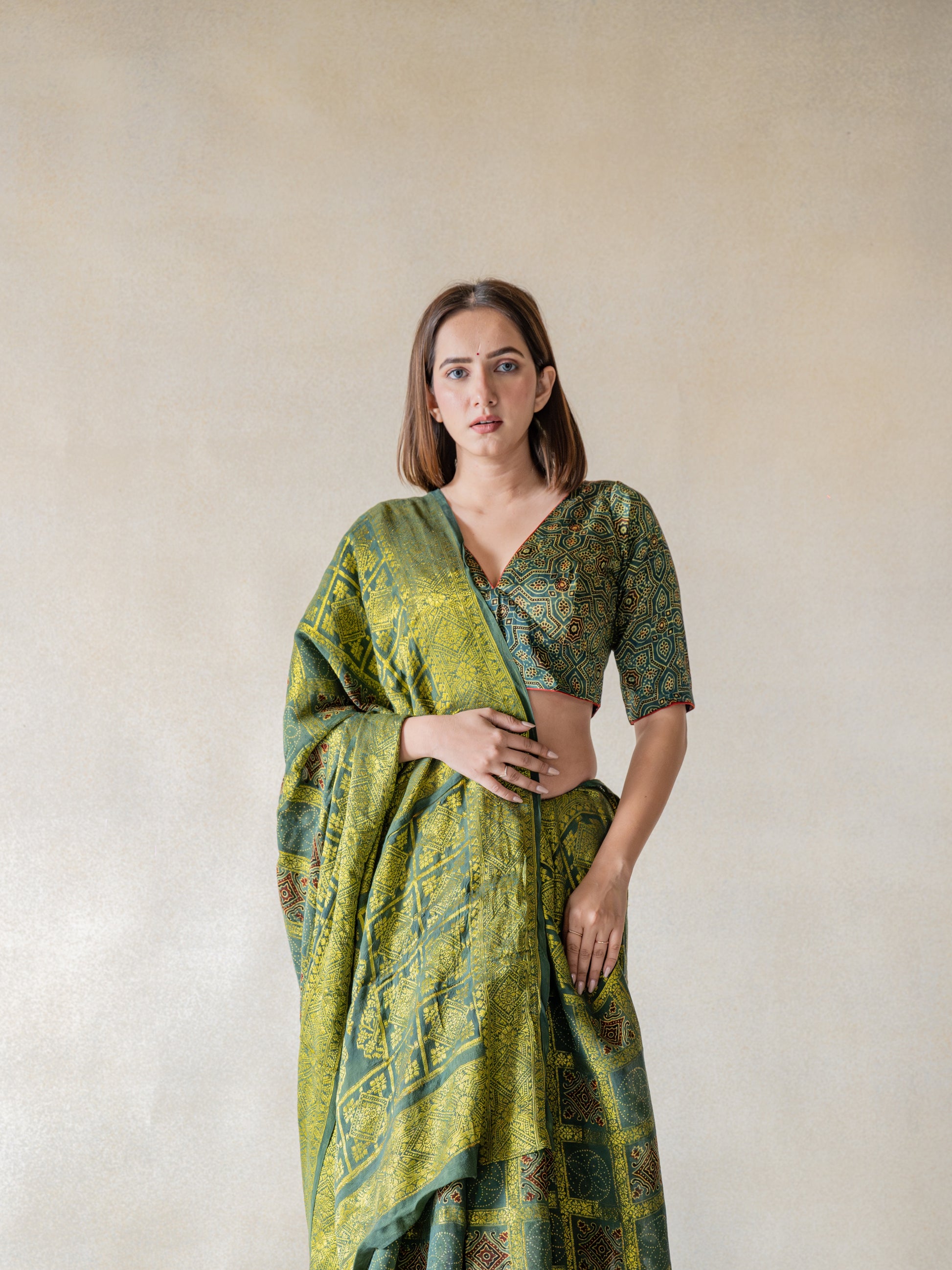 Indulge in luxury with our Green - Ajrakh Modal Silk Blouse. Handcrafted with authentic ajrakh hand block printing and natural green dyes, this blouse exudes elegance. The luxurious and comfort blend of modal silk and pure cotton lining ensure breathability and style. Slow made with intricate details, it features a charming V neck in front and button closure in the back. An exclusive piece for those who appreciate sophistication.