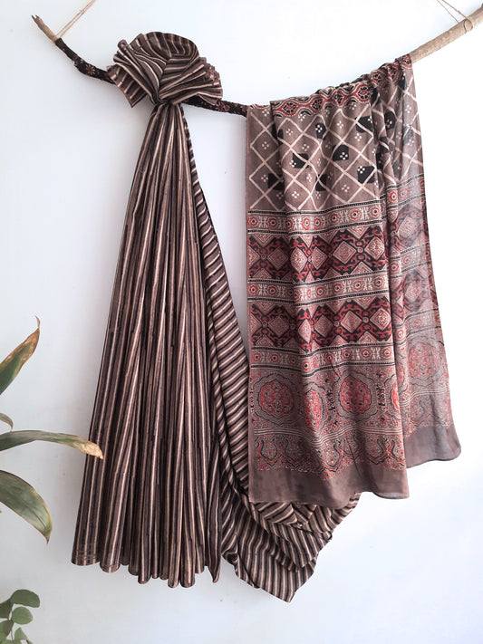 Capture the essence of Earthy Elegance with our Brown Ajrakh Hand Block Printed Saree. Intricate ajrakh hand block prints create a mesmerizing fusion of stripes and traditional patterns. Crafted from 100% cotton with natural dyes, each piece embodies lasting elegance and comfort. A wardrobe masterpiece with a touch of dedication and craftsmanship.